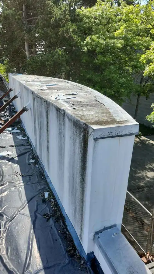 Commercial parapet wall with failed coping, black staining and torn membrane at the left, before repair