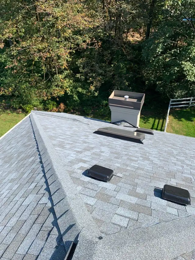 Fresh shingles, ridge, chimney cap and box vents on a finished Pacific Pride roof, trees beyond